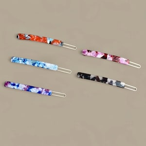 May include: Five colorful hair barrettes with a marbled design. The barrettes feature a variety of colors, including red, blue, purple, pink, and black, with a silver-tone metal clasp. These accessories are ideal for adding a touch of style to any hairstyle.