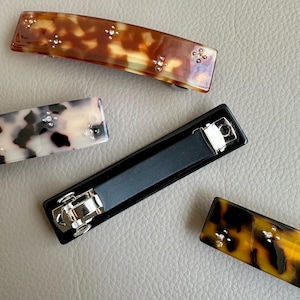 May include: Four hair clips, two are brown and black tortoise shell with rhinestones, one is black with a silver clasp, and one is white and black tortoise shell with rhinestones.