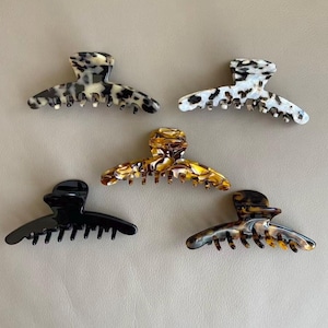 May include: Five claw hair clips in various colors and patterns. The clips include black, tortoiseshell, and speckled designs. The hair accessories are made of a glossy material and are arranged on a neutral surface.