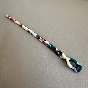 May include: A colorful hair stick with a twisted design. The stick features a pattern of red, white, green, and yellow. The hair accessory is designed to hold hair in place.