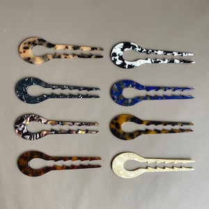 Può includere: Otto forcine decorative per capelli in vari colori e motivi. Le forcine hanno una parte superiore a forma di U con una serie di denti sul fondo e due rebbi che si estendono dalla base. I colori includono nero e bianco, blu, marrone e crema.
