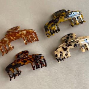 May include: Four claw hair clips in various tortoiseshell patterns. The clips feature shades of brown, tan, and black, with a glossy finish. These hair accessories are designed to hold hair in place.