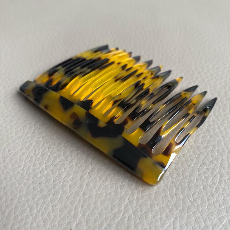 Puede incluir: Un peine para el cabello con un dise&ntilde;o curvo y un patr&oacute;n de carey. El peine presenta tonos amarillos y marrones oscuros alternados, con un acabado brillante. Los dientes est&aacute;n espaciados uniformemente y terminan en punta.