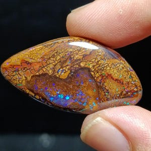 May include: A brown, iridescent opal cabochon with a unique, patterned surface. The opal displays a variety of colors, including blue, green, and red.