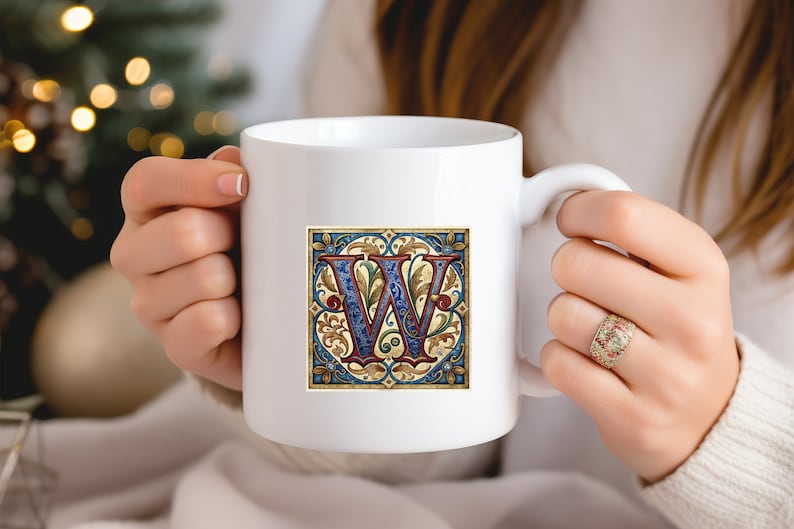 May include: White ceramic mug with a colorful illustration of the letter "W" in a decorative frame. The letter is blue and red with gold accents. The frame is blue, gold, and green.