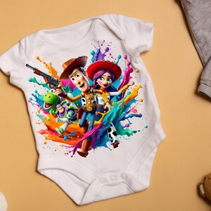 May include: White baby onesie with a colorful paint splatter design featuring Woody, Jessie, and Rex from Toy Story.