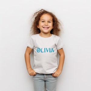 May include: A white t-shirt with a blue swirl design and the name 'OLIVIA' printed on the front.