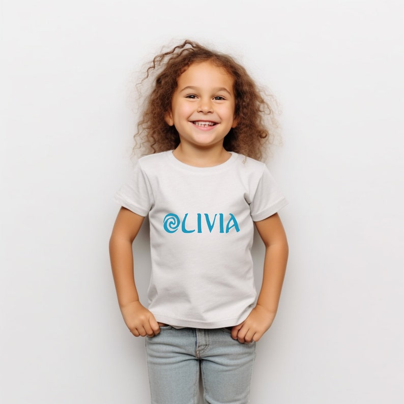 May include: A white t-shirt with a blue swirl design and the name 'OLIVIA' printed on the front.