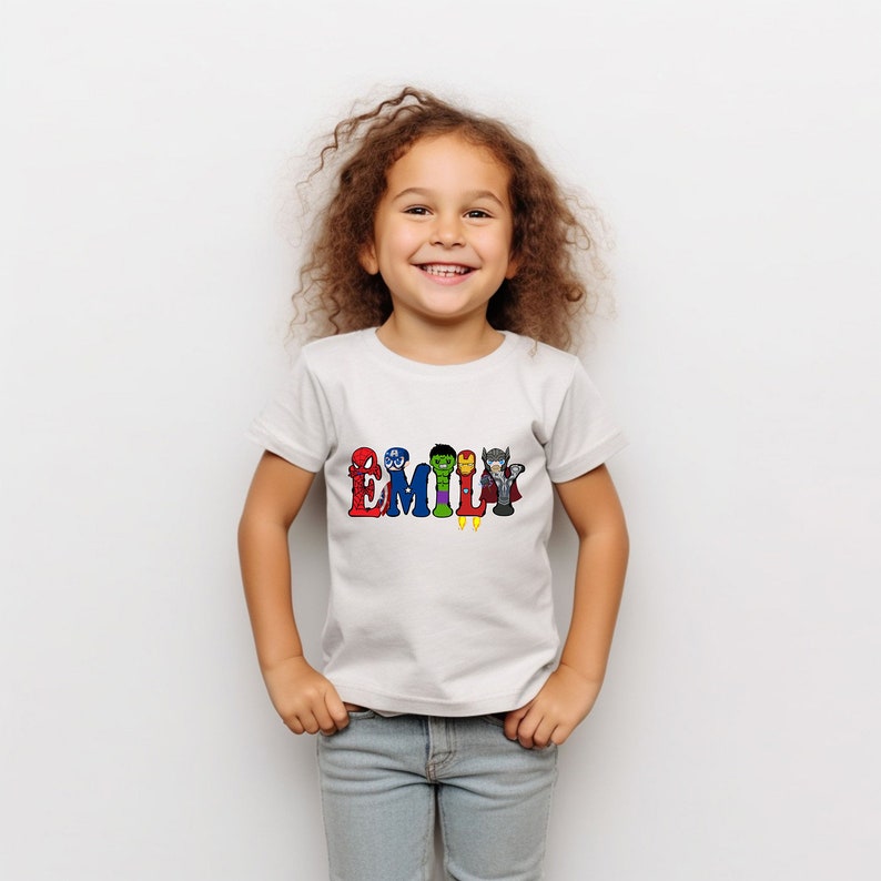 May include: White t-shirt with the name "EMILY" spelled out in colorful letters. Each letter features a different superhero character from the Avengers.