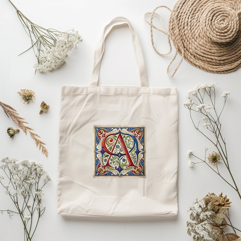 May include: A white canvas tote bag with a red, blue, and green floral design featuring the letter "A" in a decorative font. The bag has a long handle.