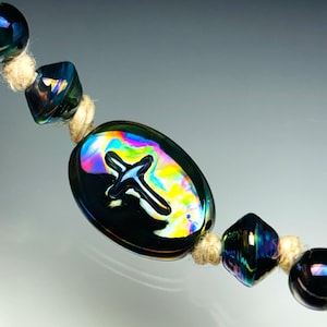 May include: A close-up of a rosary with iridescent black beads and a cross pendant. The beads are various shapes, including round, square, and oval. The cross pendant is centered on the rosary. The beads are strung on a natural-colored cord.