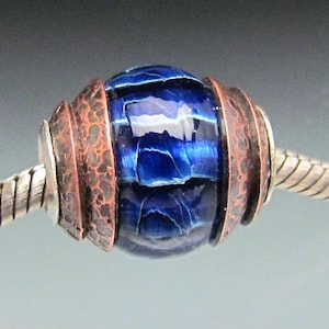 May include: A blue and copper glass bead with a textured copper finish. The bead is part of a silver chain.