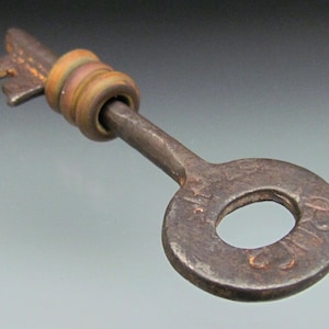 May include: A vintage-style key with a circular handle and a keyhole. The key is made of metal with a rusty, aged appearance. The key's handle has a decorative ring design. The key is likely used for decorative purposes or as a collectible item.
