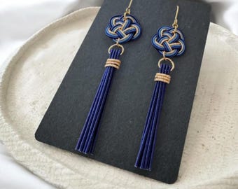 May include: A pair of blue and gold tassel earrings with a knot design. The earrings are on a black surface with the text "Sakura Style Tokyo".