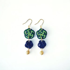 May include: A pair of dangle earrings with blue and green knotted designs. The earrings have a gold hook and a small gold bead at the bottom.