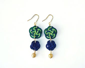May include: A pair of dangle earrings with blue and green knotted designs. The earrings have a gold hook and a small gold bead at the bottom.