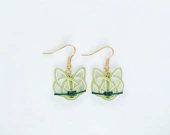 May include: A pair of light green cat-shaped earrings with gold-colored hooks. The earrings are made of woven material, with a dark green accent at the bottom. The earrings are displayed on a white background.