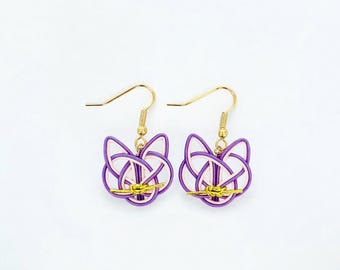 May include: A pair of handmade earrings featuring a cat-like design. The earrings have a purple and white pattern with gold-colored hooks. The earrings are displayed on a white background.