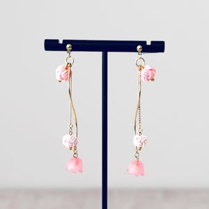 May include: A pair of pink and white dangle earrings with a gold chain and pink flower charms.