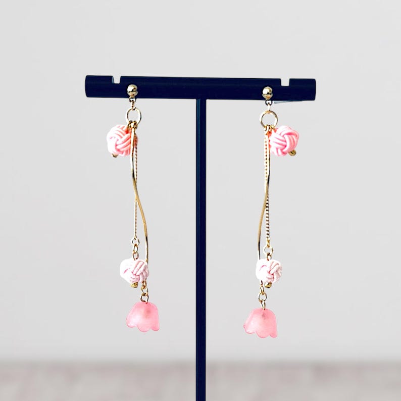 May include: A pair of pink and white dangle earrings with a gold chain and pink flower charms.