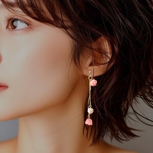 May include: A pair of long, delicate earrings with a gold chain and pink flower accents.