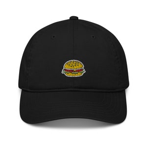 May include: Black baseball cap with an embroidered image of a yellow hamburger with lettuce, tomato, and sesame seeds.