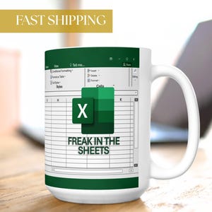 May include: White ceramic mug featuring a green and white Excel spreadsheet design with the Microsoft Excel logo and the text "FREAK IN THE SHEETS." The mug has a white handle and is set against a blurred background.