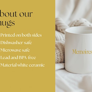 May include: A white ceramic mug with the word "Memoires" in gold lettering. The mug is on a white surface with a knitted blanket in the background. The image also includes text that says "About our mugs" and lists features like being dishwasher and microwave safe.