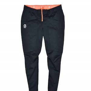 May include: Black athletic pants with an orange waistband and drawstring. The pants have a white logo on the left leg and are designed for outdoor activities. The pants are made of a durable, water-resistant material.