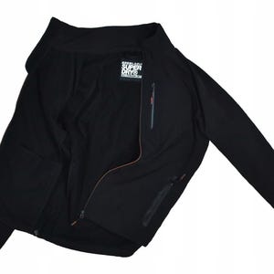 May include: Black zip-up jacket with a high collar and long sleeves. Features a chest pocket with a vertical zipper and a small tag with the text "SUPER DRY". The jacket has a sleek, minimalist design.