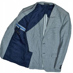 May include: A gray blazer with a navy blue interior. The blazer has a two-button closure, a chest pocket, and a white stripe detail on the lapel. The interior lining is a solid navy blue.