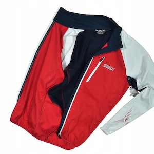 May include: A red, white, and navy blue athletic jacket with the brand name "SWIX" printed on the front. The jacket has a full zipper and a white stripe down the side. The jacket is designed for outdoor activities.