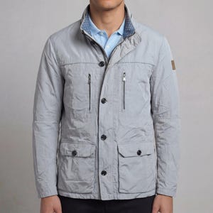 May include: A light gray jacket with a button-up front, two chest pockets, and two lower pockets. The jacket has a zip pocket on each side of the chest and a small brown patch on the right sleeve. The collar has a blue and white polka dot lining.