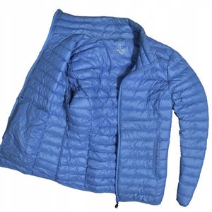 Puede incluir: Chaqueta acolchada azul claro con cremallera completa. La chaqueta tiene cuello alto y dos bolsillos laterales. El forro interior es del mismo color azul claro que el exterior. Un pequeño logotipo es visible en el pecho.