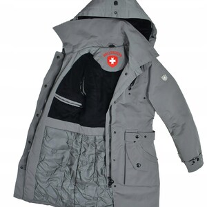 May include: A grey winter coat with a hood, black lining, and quilted lower section. It has a zip closure, multiple pockets, and a red and white logo inside. The coat is designed for cold weather, with a length that extends to the mid-thigh.