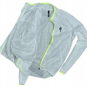 May include: A white, lightweight cycling jacket with neon yellow trim along the zipper, collar, and cuffs. The jacket has a full-length zipper and a small black logo on the chest. The jacket is open, showing the interior lining.