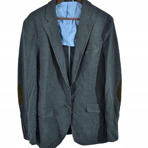 May include: A gray blazer with brown elbow patches and a light blue lining, hanging on a wooden hanger. The blazer has two front pockets and a two-button closure. The sleeves have four buttons.