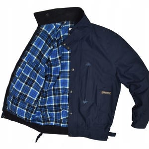 Könnte beinhalten: Marineblaue Jacke mit schwarzem Kragen und blauem, schwarz-weißem Karofutter. Die Jacke hat einen Knopfverschluss, eine kleine Tasche und einen Logoaufnäher. Ein klassisches Oberbekleidungsstück.