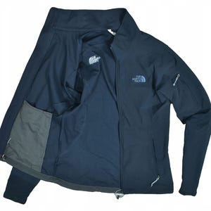 May include: A navy blue The North Face jacket with a full zipper and long sleeves. The jacket has a small logo on the chest and a mesh pocket on the inside. The jacket is open, revealing the interior lining.
