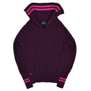 May include: A dark purple sweater with a zip-up collar and pink stripes on the collar and cuffs. The sweater has a ribbed texture and a small logo near the cuff. The brand name is visible on the label.
