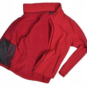 May include: A bright red jacket with a full zipper closure and a high collar. The jacket has a mesh pocket on the inside and a small logo on the sleeve. The jacket is open, showing the interior lining.