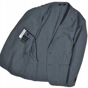 May include: A gray blazer with a two-button closure, a notched lapel, and a chest pocket. The inside of the blazer has a tag with text. The blazer is made of a woven fabric.