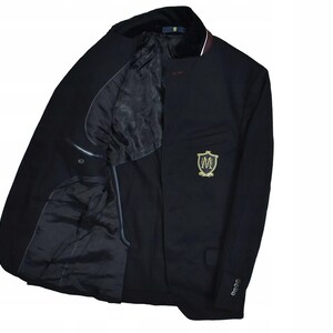 May include: A navy blue blazer with a black velvet collar and a gold embroidered crest on the chest. The blazer has a two-button closure and a satin lining. The inside pockets are visible. The blazer is a classic style.