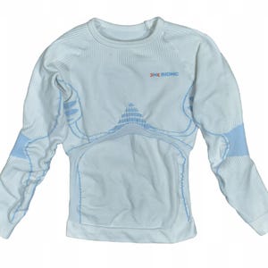 Puede incluir: Una camiseta deportiva blanca de manga larga con detalles en azul claro. La camiseta de cuello redondo presenta un diseño en el pecho y las mangas. La marca "BIONIC" está impresa en el pecho.