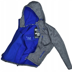 Peut inclure: Veste à capuche grise avec un intérieur bleu vif. La veste a une fermeture éclair, plusieurs poches et le texte "Superdry" sur une étiquette. La veste est faite d'un matériau doux et texturé.