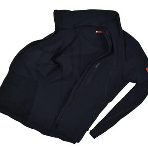 May include: A black zip-up jacket with a high collar. The jacket has a red logo patch on the sleeve and a zipper closure. The interior of the jacket is visible, showing the lining and pockets. The jacket is made of a smooth, matte material.