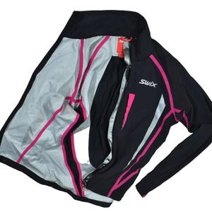 May include: Black and pink athletic jacket with the brand name "Swix" on the chest. The jacket has a full zipper, long sleeves, and pink accents along the seams and pockets. The interior is light gray.