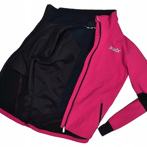 May include: A bright pink and black athletic jacket with a full zipper and the brand name "Swix" in silver. The jacket has a high collar and black accents on the sleeves and interior. The jacket is open, revealing a black interior.