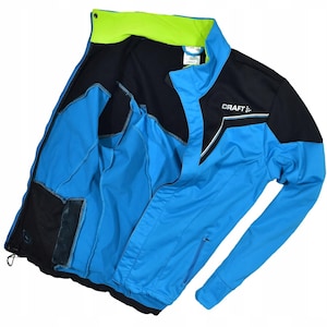 May include: A blue and black athletic jacket with the word "CRAFT" printed on the chest. The jacket has a neon green collar and interior lining. It features a zipper closure and two side pockets.