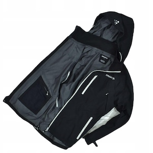 May include: Black jacket with a hood, featuring white accents and the "CRAFT" logo. The interior is gray, with a black pocket. The jacket is open, displaying the inner lining and zipper details. A sporty, outdoor apparel item.